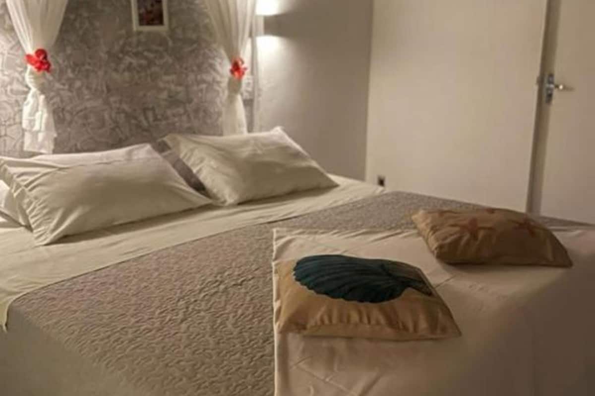 A bedroom with a bed, white curtains, a stone wall, and a door.
