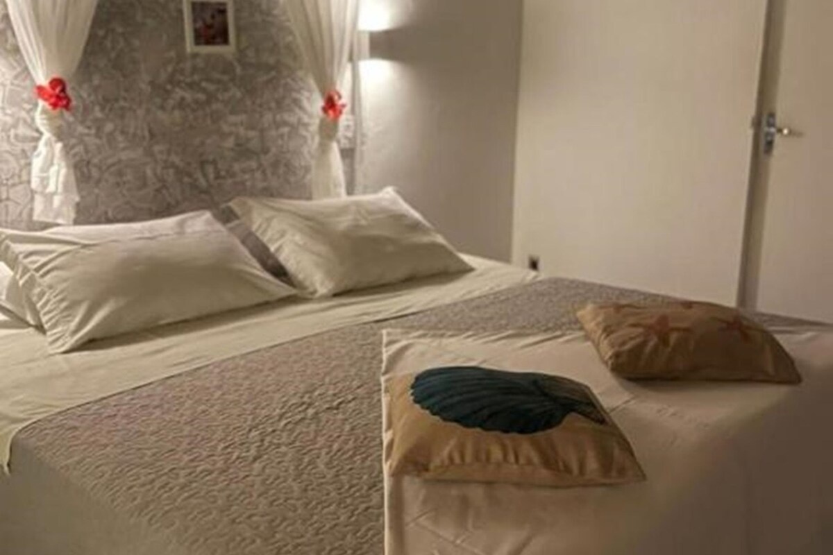 Une chambre à coucher avec un lit, des rideaux blancs, un mur en pierre et une porte.