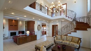 A spacious living area with a fireplace, a sofa set, a coffee table, and a staircase leading to an upper floor. - Private Heated pool★Close to the Beach★BBQ & Wifi (Galatas)