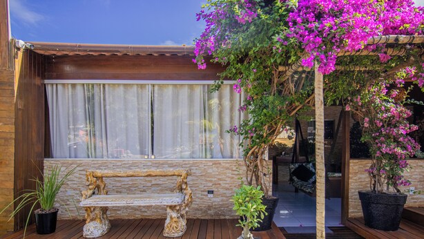A wooden deck with a bench, potted plants, and a pergola with flowering vines. - Pousada da Leide (Fernando de Noronha)