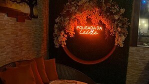 A cozy seating area with a wicker sofa and cushions, a neon sign reading "POUSADA DA Leide", and a decorative floral arrangement. - Pousada da Leide (Fernando de Noronha)