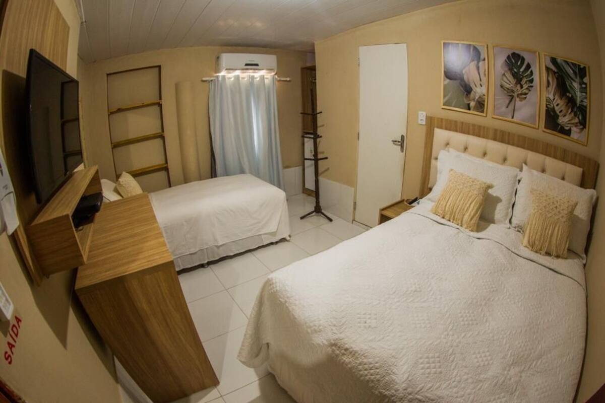 Quarto de hotel com duas camas, televisão, mesa de trabalho e janela com cortinas.