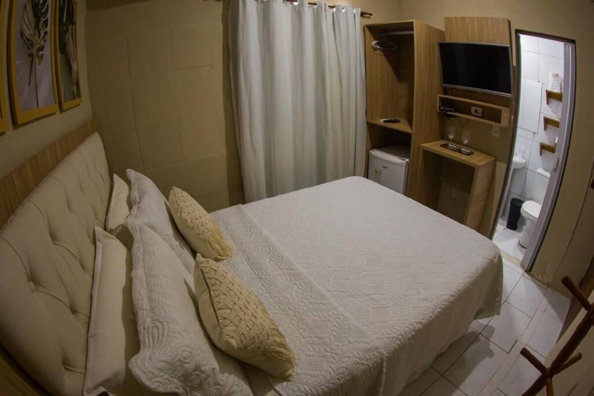 Quarto com cama, televisão, área de chuveiro e sanitário.