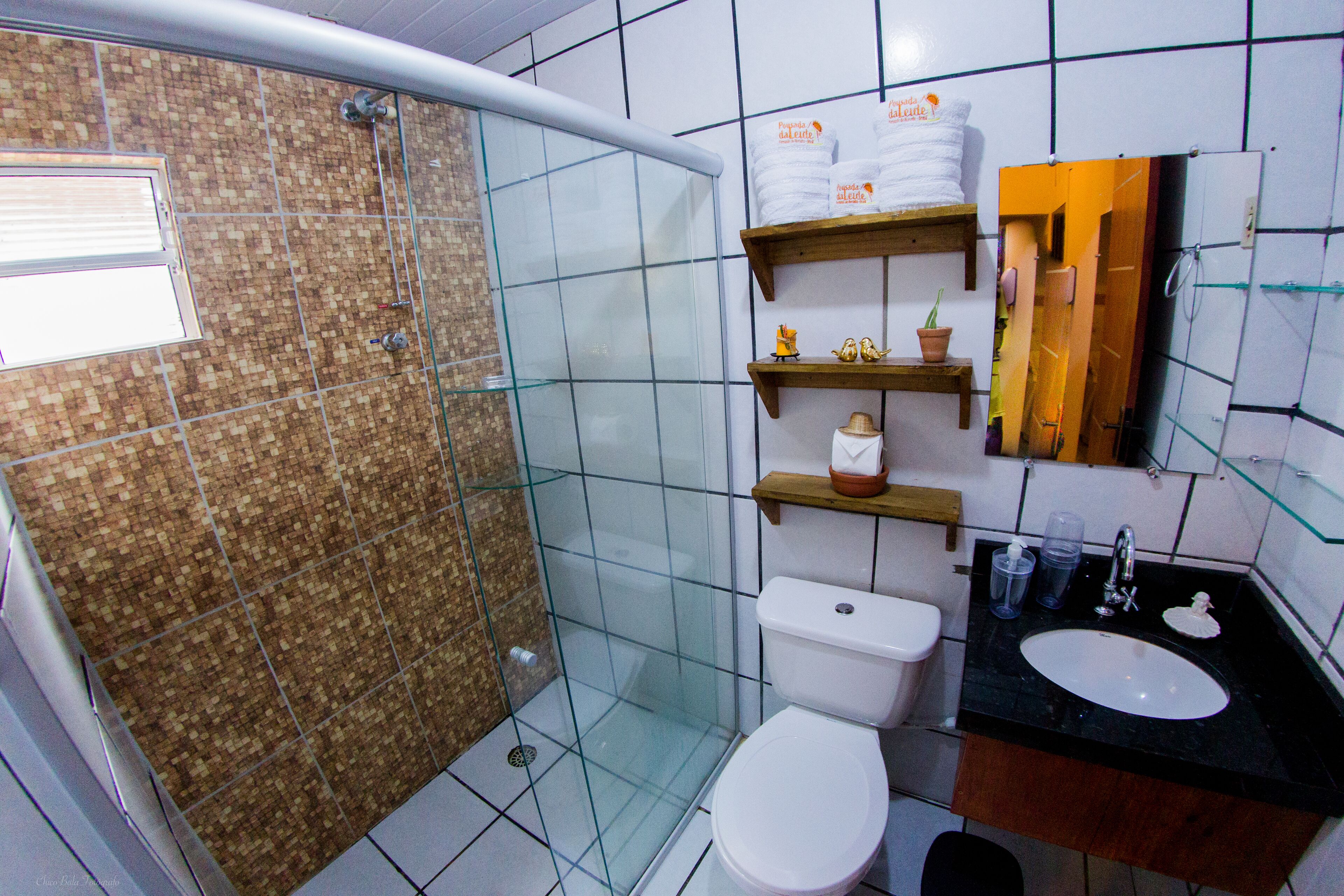 A bathroom with a glass-enclosed shower, a white toilet, a black sink, and shelves with toiletries.