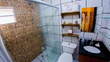 A bathroom with a glass-enclosed shower, a white toilet, a black sink, and shelves with toiletries.