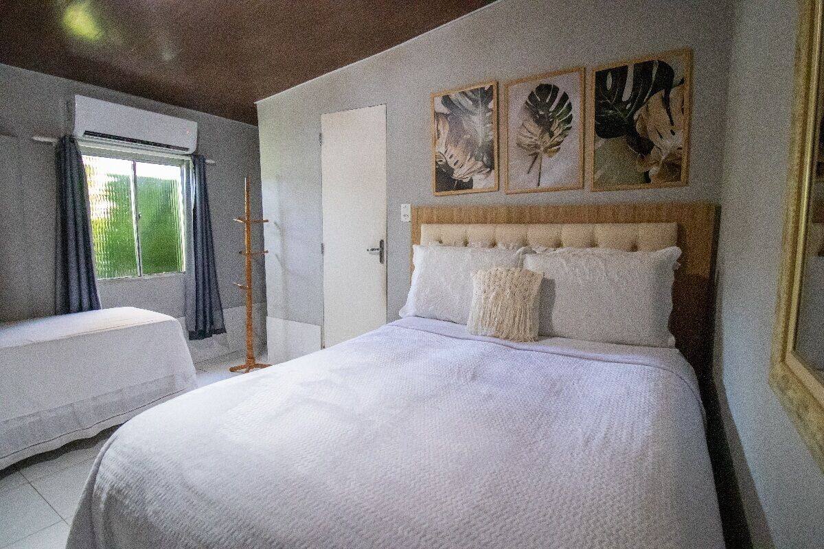 Quarto com cama, mesa de cabeceira, janela com cortinas e obra de arte na parede.