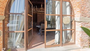 A rustic building with a brick exterior and large arched windows. Inside, there is a wooden table and chairs, and a chandelier.