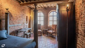 A room with exposed wooden beams, brick walls, a bed, a table with chairs, and a door with a light fixture.