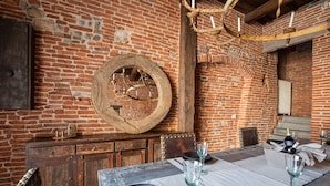 A rustic dining area with a brick wall, wooden furniture, and a large wooden wheel.