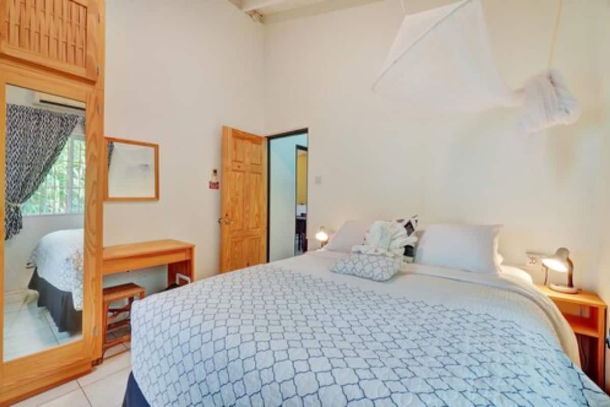Un dormitorio con cama, mesitas de noche, armario y una puerta que da a otra habitación.