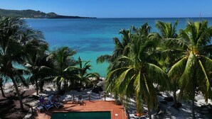 A pool area with a view of the ocean, surrounded by palm trees and lounge chairs. - Hideaway Apartments Grenada (St. George's)