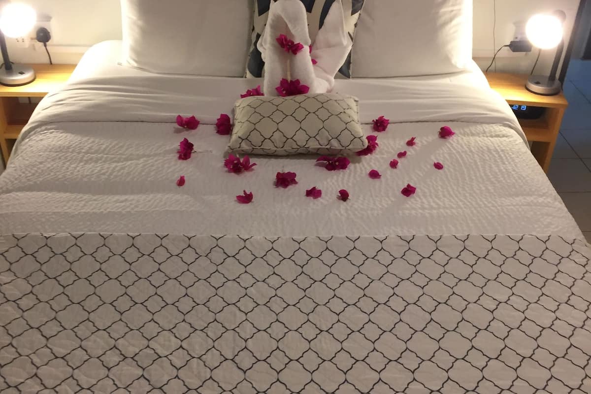 Una cama bien hecha con una colcha estampada, una almohada decorativa y pétalos de rosa dispersos.