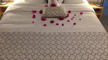 A neatly made bed with a patterned bedspread, a decorative pillow, and scattered rose petals.