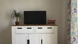 Un meuble blanc sur lequel est posée une télévision, avec une plante en pot et une pile de livres à côté.