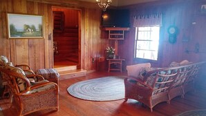 L’intérieur d’un chalet en bois, avec des meubles en osier, un téléviseur et un tableau accroché au mur.