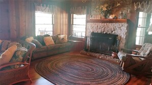 Un salon chaleureux avec une cheminée, des murs en bois et un canapé agrémenté de coussins à motifs.