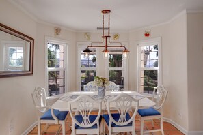 A dining room with a white table and chairs, a vase with flowers, and a view through large windows. - French country ranch in the heart of wine country with a new spa (Temecula)