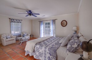 Ein Schlafzimmer mit einem Bett, einem Sofa, einem Couchtisch, einem Deckenventilator und einem Fenster mit Vorhängen.