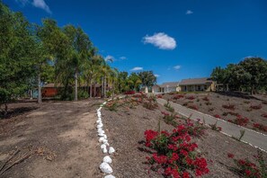 A residential area with houses, a dirt path, and red flowering plants. - French country ranch in the heart of wine country with a new spa (Temecula)