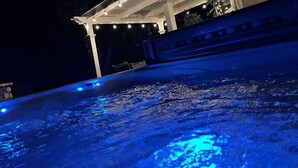 Uma banheira de hidromassagem com iluminação azul, uma pérgula com luzes de cordão e uma parede de pedra.
