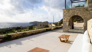 A terrace with a stone wall, a wooden table, and a white sofa overlooking the sea.