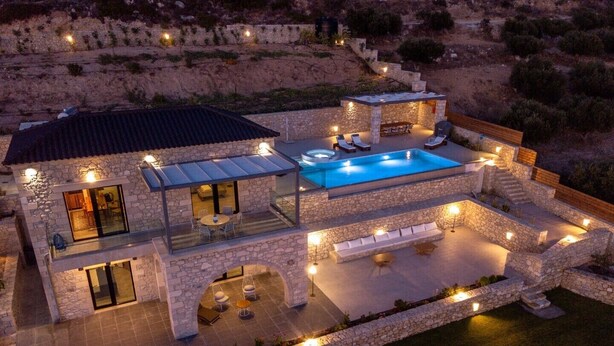 A two-story stone house with a swimming pool, outdoor seating, and a stone staircase.