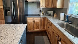 Una cucina con mobili in legno, frigorifero in acciaio inossidabile, piani in granito e una finestra con persiane.