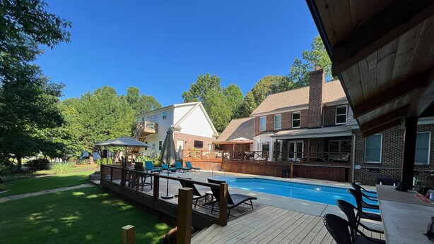 Un giardino con un patio in legno, una piscina e mobili da esterno.