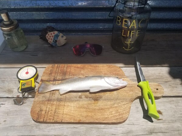 Una tabla de madera con un pescado, un cuchillo, una balanza y una botella de agua sobre una superficie de madera.