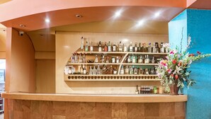 A bar area with multiple shelves of liquor bottles and a vase of flowers. - Capital O Andrade, Mexico City (Mexico City)
