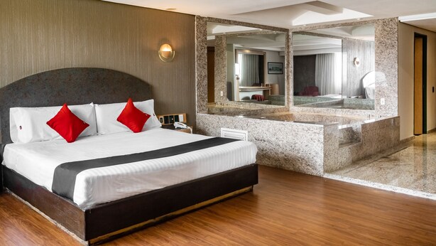 A modern hotel room with a large bed, a built-in vanity with a mirror, and a wooden floor. - Capital O Andrade, Mexico City (Mexico City)