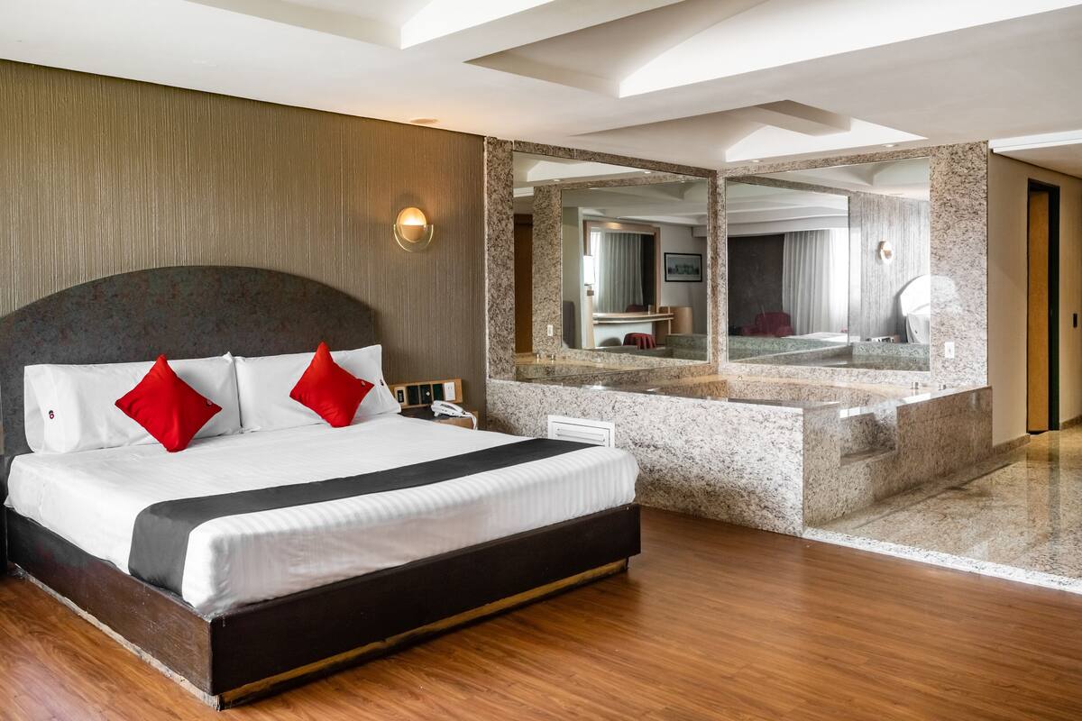 A modern hotel room with a large bed, a built-in vanity with a mirror, and a wooden floor.