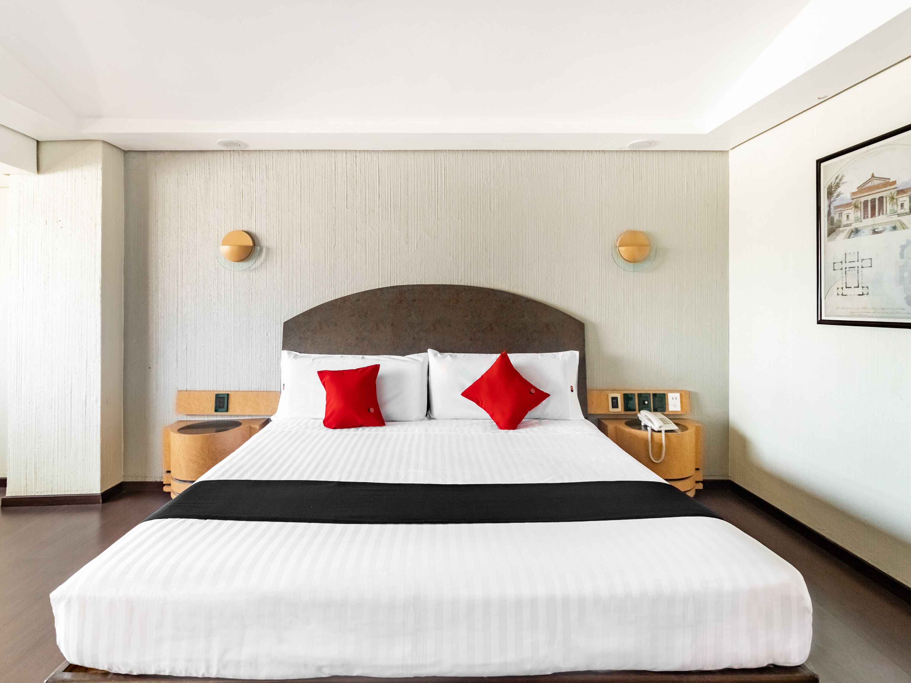 Una habitación de hotel con una cama grande, dos mesitas de noche, un teléfono de pared y un cuadro en la pared.