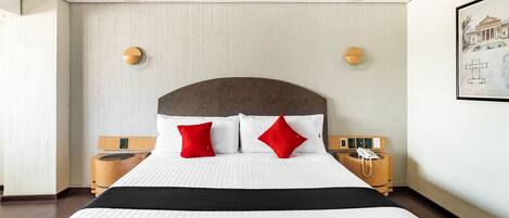 Una habitación de hotel con una cama grande, dos mesitas de noche, un teléfono de pared y un cuadro en la pared.