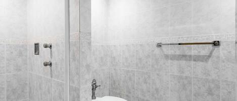 Un baño moderno con cabina de ducha de vidrio, inodoro y barra de apoyo.