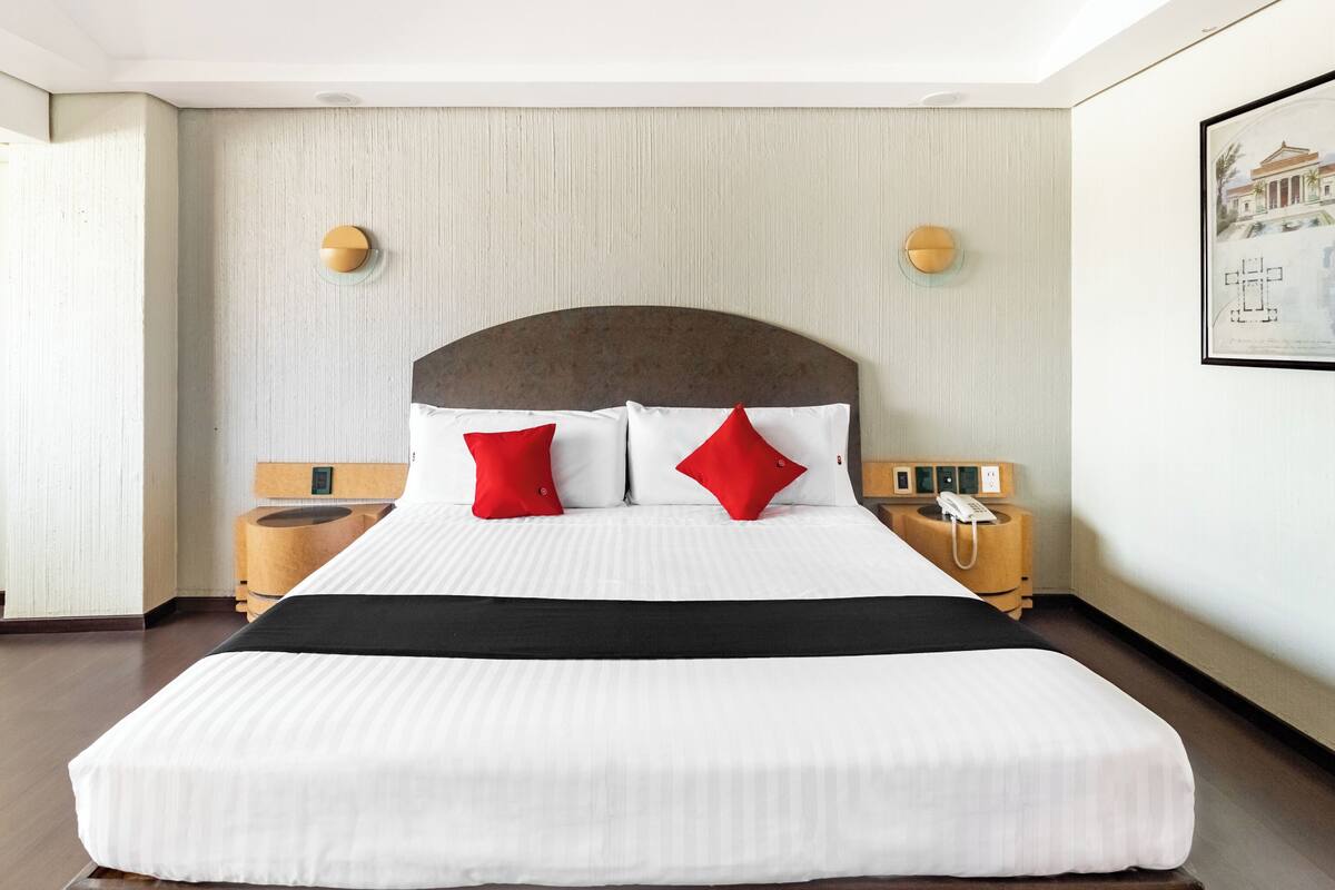 A hotel room with a large bed, two bedside tables, a wall-mounted phone, and a framed picture.