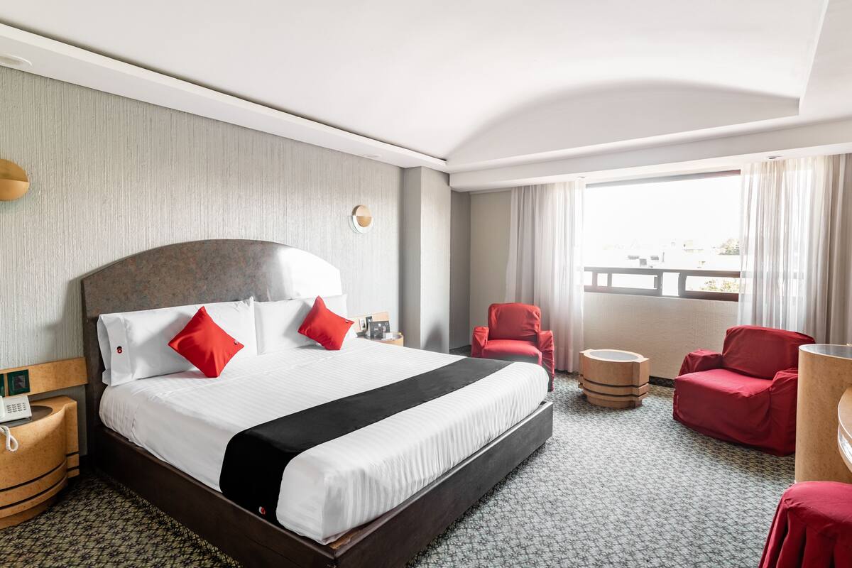 A hotel room with a large bed, a desk, a chair, and a view of the city.
