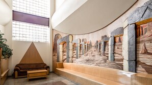 A lobby with a stone wall mural, a wooden bench, and a brown sofa. - Capital O Andrade, Mexico City (Mexico City)
