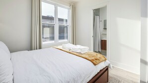 Une chambre à coucher avec un lit, une fenêtre avec des rideaux, un miroir et une vue sur l’extérieur.