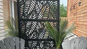 Une terrasse avec deux fauteuils Adirondack et une petite table, entourée d’une clôture décorative en treillis noir et de plantes en pot.