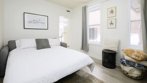 Un dormitorio con una cama grande, una mesita de noche, una ventana con cortinas y un cuadro en la pared.