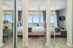 A bedroom with a large bed, a TV, and a view of the ocean. - Dolphin Beach H106 (Cape Town)