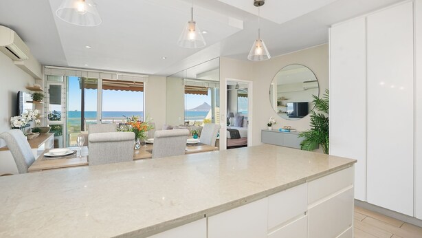 Cozinha moderna com uma ilha grande, iluminação pendente e vista para o mar.