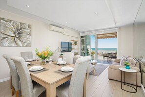 A modern living room with a dining area, a television, and a view of the beach. - Dolphin Beach H106 (Cape Town)