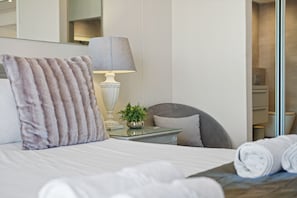 A neatly made bed with a fluffy pillow, a bedside lamp, and a small potted plant. - Dolphin Beach H106 (Cape Town)