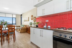 A modern kitchen with white cabinets, a red tiled backsplash, and a large window overlooking a scenic view.