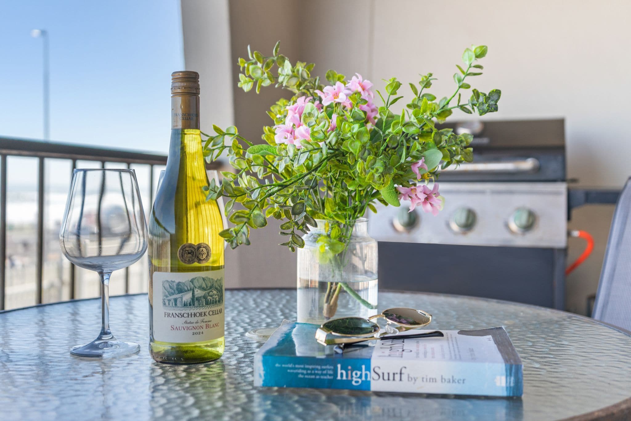 En vinflaska, ett vinglas, en bok och en vas med blommor på ett bord.