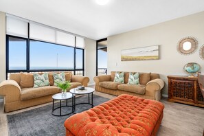 A spacious living room with two sofas, a coffee table, and a large ottoman. There is a globe and a decorative mirror on a wooden side table.