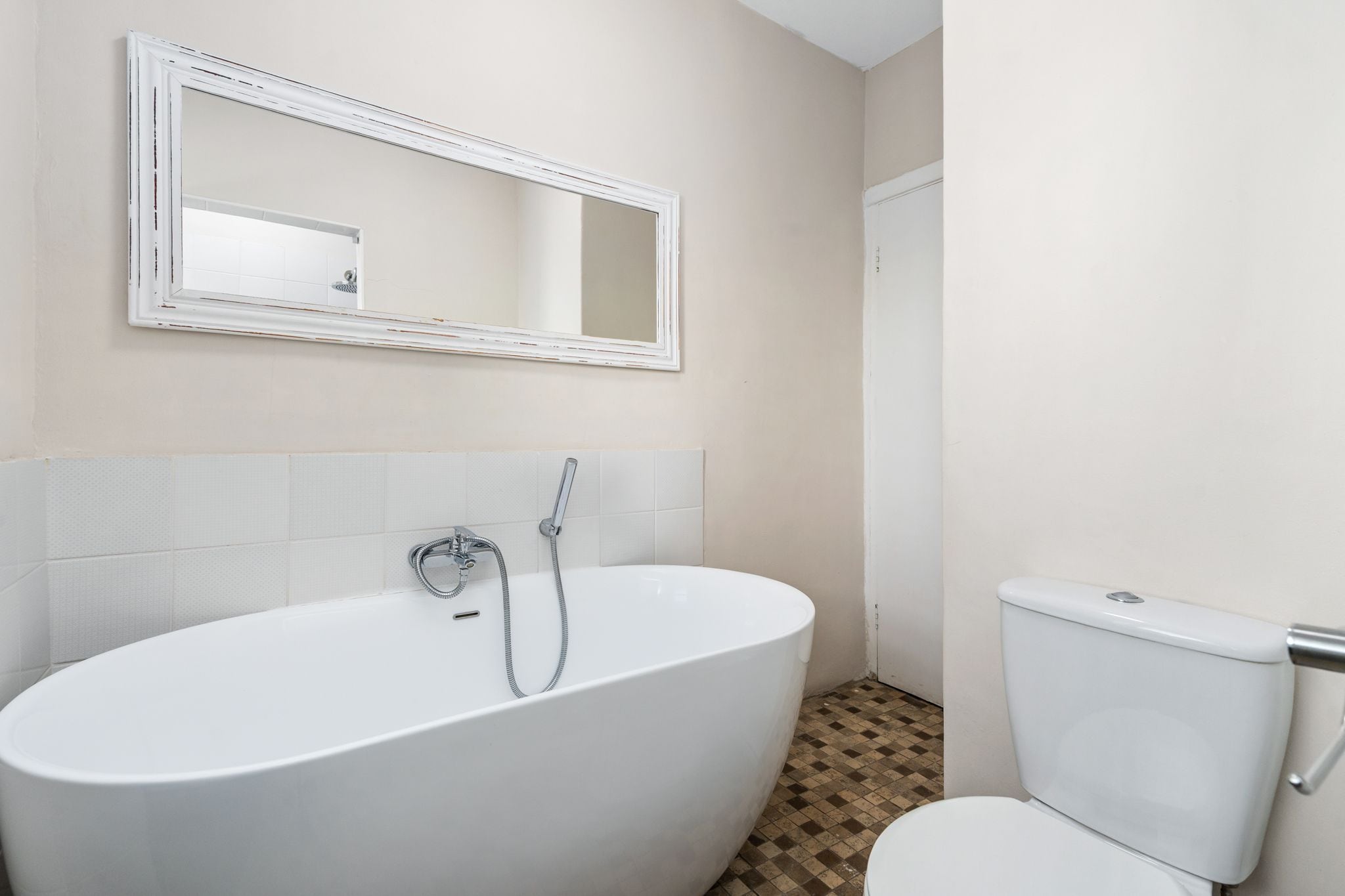 A bathroom with a freestanding bathtub, a toilet, and a mirror on the wall.
