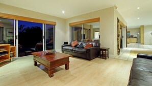 A spacious living room with a large sofa, a wooden coffee table, and a sliding glass door leading to an outdoor area. - Durham Close 31 (Cape Town)